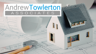 Model house stood on top of planning drawings. Ruler and pencils in foreground and rolls of plans in the background